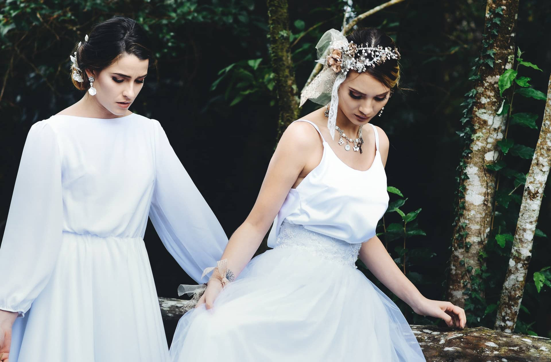 two women in wedding dresses walking through a green forest